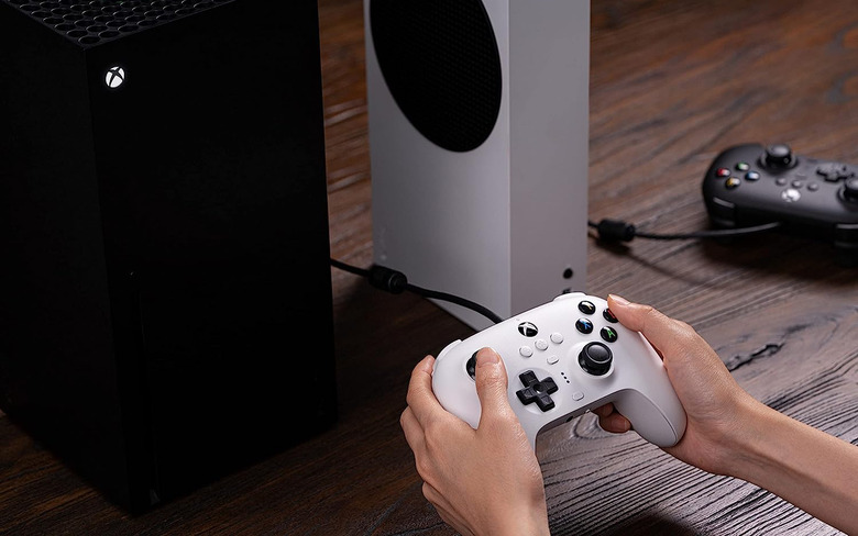 Hands holding a controller with an Xbox on top of a wooden table.