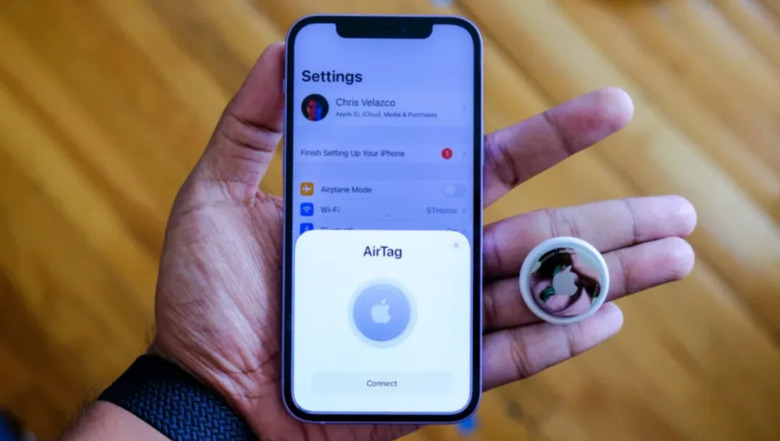 An AirTag, an iPhone and a hand.