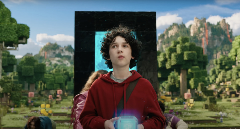 A still from A Minecraft Movie showing Sebastian Hansen as Henry entering the Minecraft world holding a glowing blue block