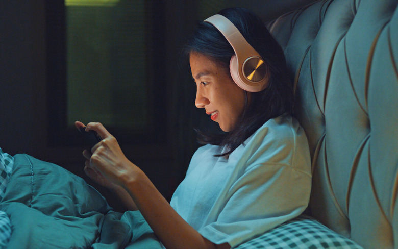 Young Asia girl media addiction on bed wear headphone laugh watch favorite movie in streaming online VOD, video on demand in home at night. Insomnia, Cybersickness, Nomophobia, sleep disorder concept.