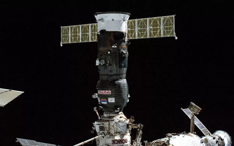 Image of a Russian Progress supply craft docked with the International Space Station, with the black of space in the background.