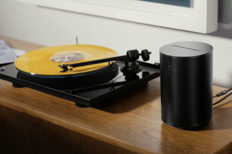 Sonos Era 100 in black on a wooden shelf next to a turntable