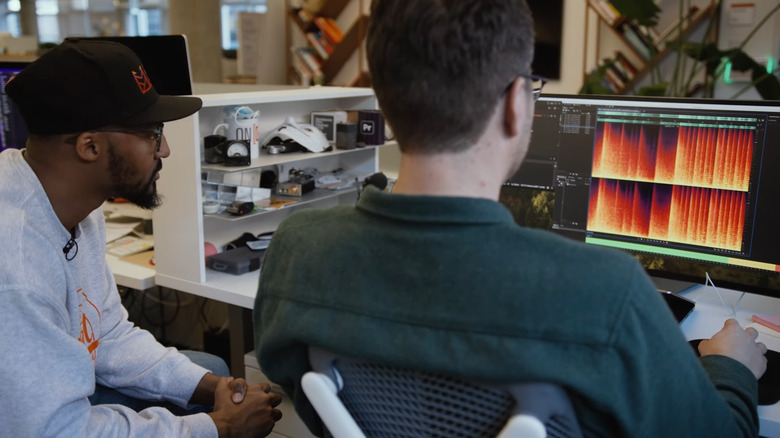 Still from a promotional video showing two people sitting in an office, looking at a computer screen, creating music with AI.