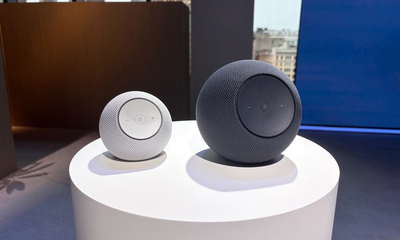 Two speakers, a white Amazon Echo Dot Max and gray Amazon Echo Studio, sit on a white podium on a black stage.