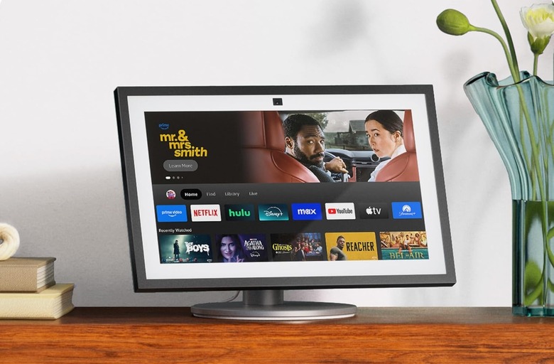 Amazon's Echo Show 15 smart display pictured on a wooden surface next to a a vase and a stack of books