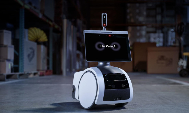 Security robot (screen with wheels and a periscope) sitting in a dark warehouse.