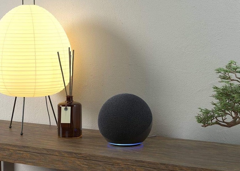 An Echo Show sits on a wooden table beside a diffuser and lamp.
