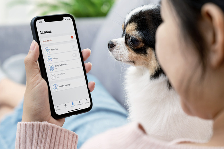 A person holding a phone showing the interface of a diabetes care app, with a dog next to them.