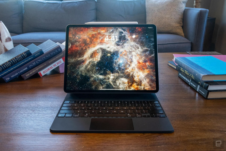 An iPad Pro with a dynamic galaxy wallpaper sitting on a desk with books. A couch looms behind it.