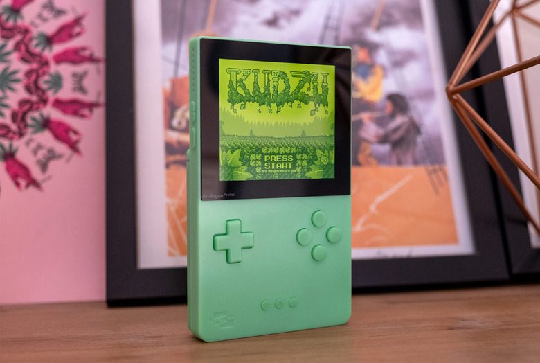 A special edition Analogue Pocket in green is pictured on a shelf with a game onscreen.