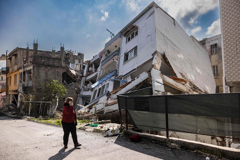 A pedestrian uses a smartphone as she walks past a collapsed building in Antakya, southern Turkey on February 21, 2023. - A 6.4-magnitude earthquake late February 20, rocked Turkey's southern province of Hatay and northern Syria, killing six people and sparking fresh panic after a massive February 6 tremor left nearly 45,000 dead in both countries. (Photo by Sameer Al-DOUMY / AFP) (Photo by SAMEER AL-DOUMY/AFP via Getty Images)