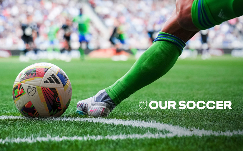 A soccer ball and the leg of a player on the grass.