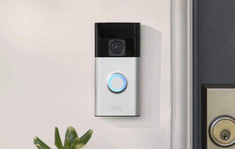 A Ring doorbell pictured on a light colored wall next to a door lock