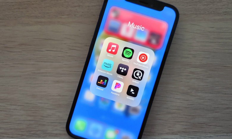A smartphone lies on a desk, displaying icons for several music streaming apps.