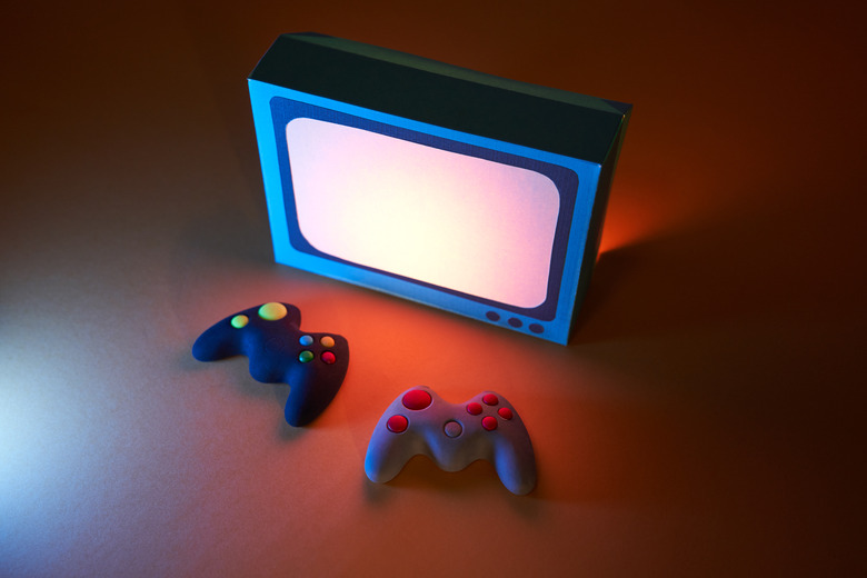 High angle view of two game controllers in front of a retro-style television. The screen light illuminates the game controllers. Video games concept.