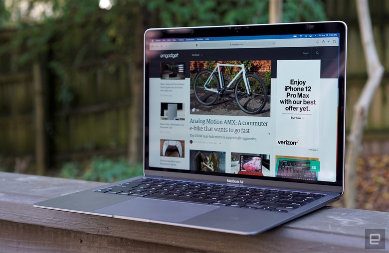 A MacBook Air laptop perched on top of a wooden baluster with trees in the background.                                
