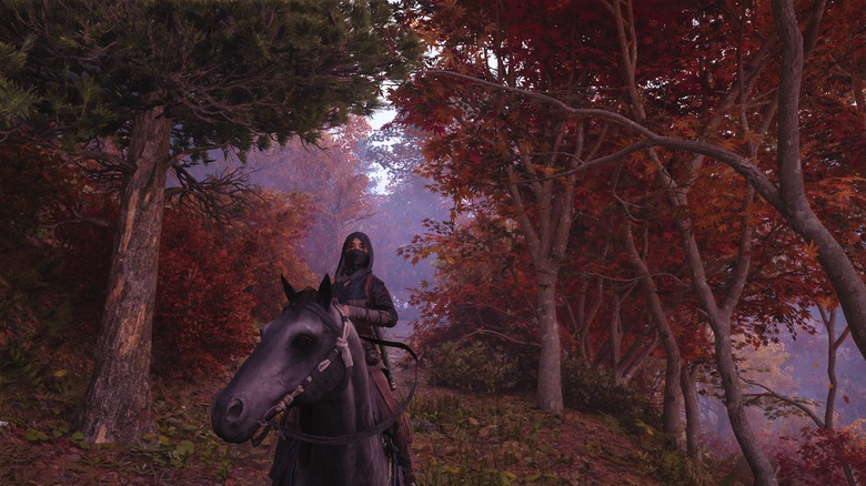A masked and hooded figure sits on a horse among some trees with brown and golden leaves.