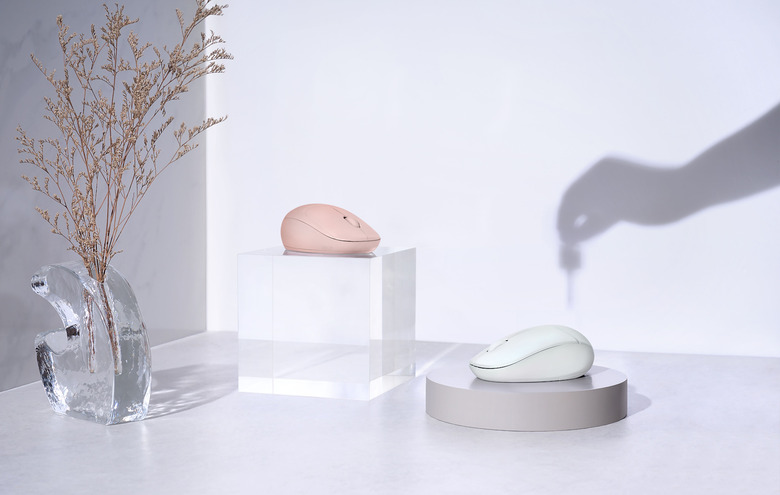 A pink and white mouse on a table with the shadow of a hand holding a dropper in the background.