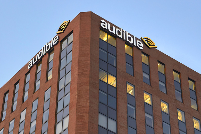 View from below of the top corner of Audible’s headquarters. The brown-red brick building has Audible logo signs on either side of the corner.