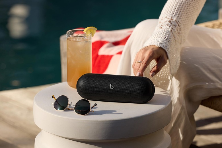 A black Beats Pill speaker on a small outdoor table with sunglasses and an iced beverage. 