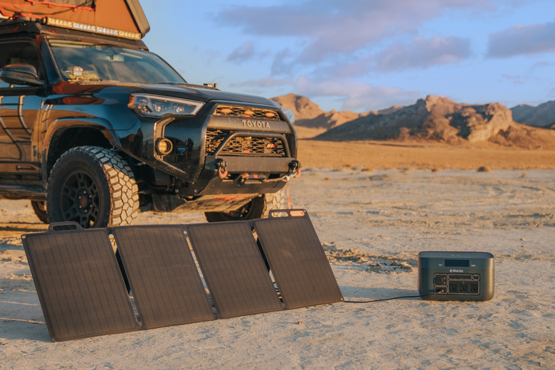 An SUV parked in a remote desert-like area has the BioLite BaseCharge 1500 and SolarPanel rigged to collect a charge from the sun.