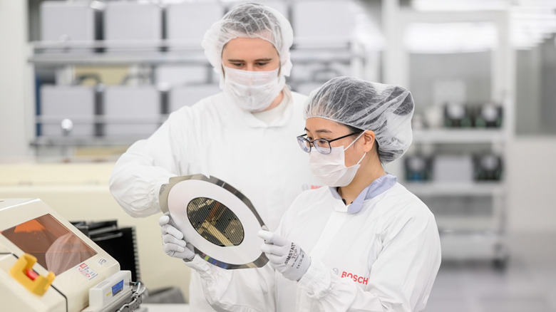 Lab workers wearing masks hold something in a semiconductor lab.