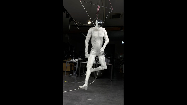 A white, muscle-y robot kicking its legs on a hook.