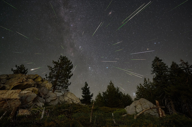 Streaks of light from the Perseid meteor shower are seen over a mountain landscape with boulders and trees