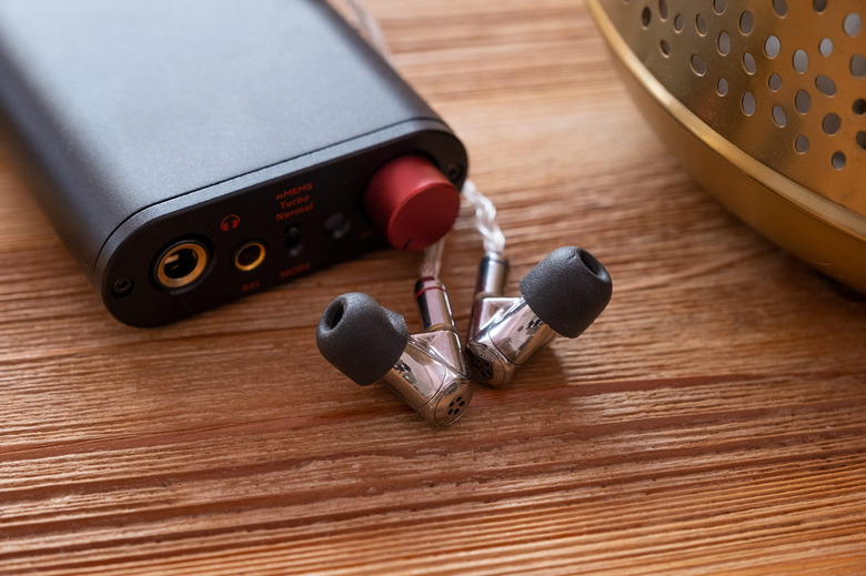 A pair of silver headphones are pictured infront of a hi-fi DAC on top of a coffee table.