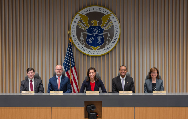 Five people sitting at a table with the logo of the Federal Communications Commission behind them.