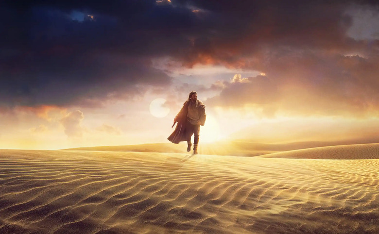 A still from the Disney+ show 'OBI-WAN KENOBI' showing Obi-Wan walking alone over sand dunes with dramatic dark clouds along with a bright late evening (or early morning) sun in the sky.