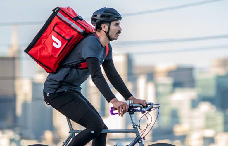 A person wearing a red backpack thermal bag with the DoorDash logo.