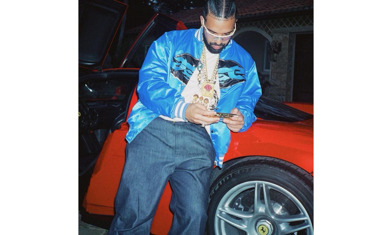 The rapper Drake leaning against a red car, looking at his phone.