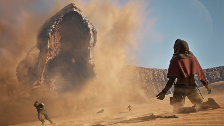 Still from the upcoming game Dune: Awakening. The hero (view from behind) kneels while watching a giant sandworm in the background. Some dude is running from it.