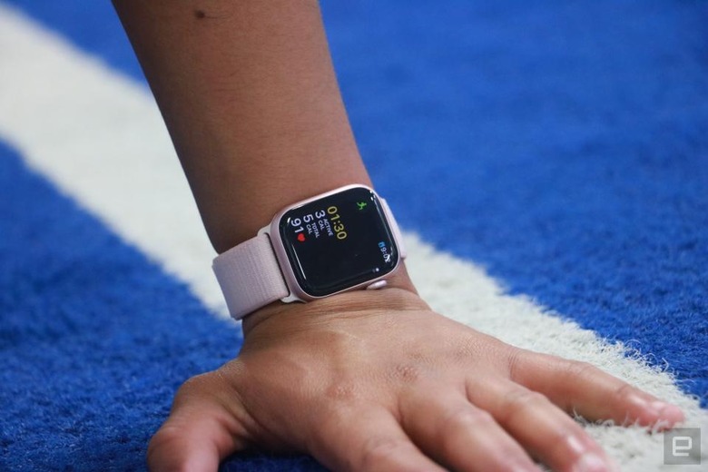 Closeup of a person’s left hand on a track's starting line. They wear the Apple Watch Series 9 on their wrist with a tracked workout on its screen.