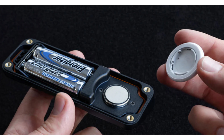 Hands holding a device with two AA batteries and part of an AirTag.
