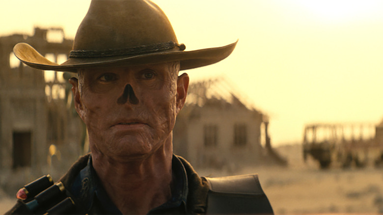Closeup of Walton Goggins as The Ghoul in Prime Video’s Fallout series. He stares pensively in front of an abandoned town in a desert wasteland.