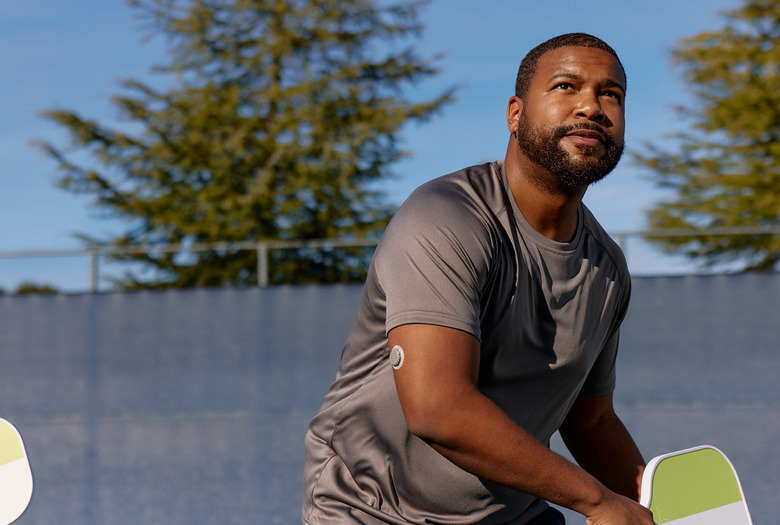 A man wearing gray shirt and holding a pickleball racket with a patch on his arm.