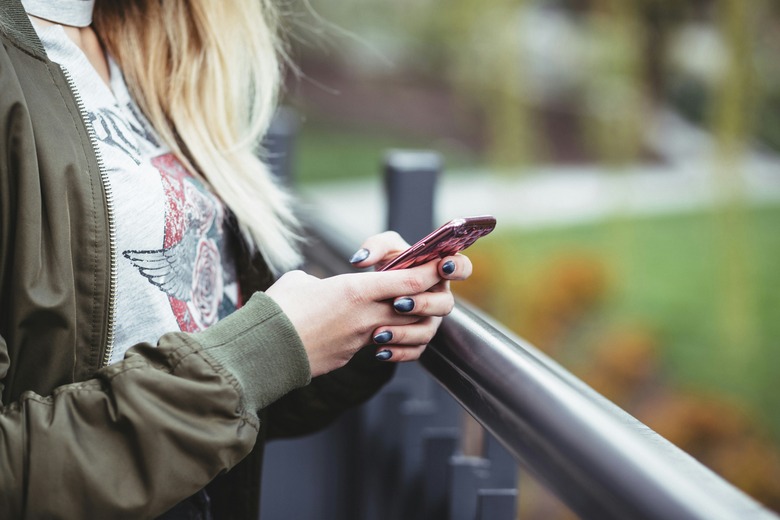 The torso of what appears to be a young woman holds a smartphone while standing next to a railing.