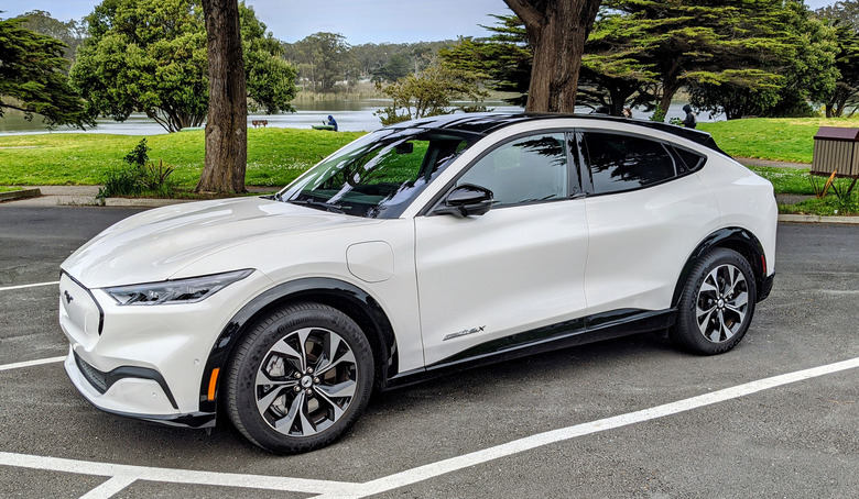 The Ford Mach-E EV in white parked in a lot by a park.