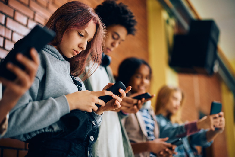 High school student and her friends using their smart phones in a hallway.