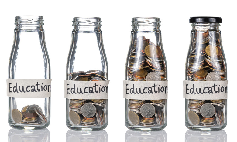 Four glass bottles sitting next to each other with growing stacks of coins inside of them. Each bottle has a piece of tape on it that says 