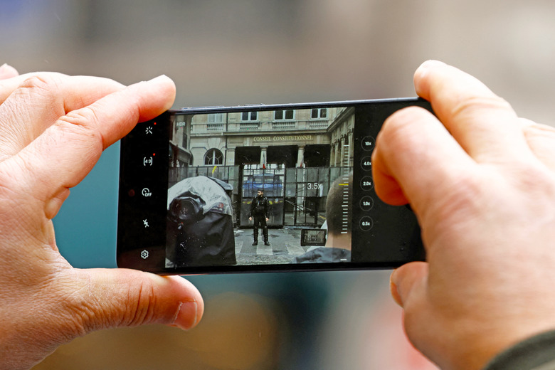 A man takes a picture with his mobile phone as French gendarmes block the access to the Constitutional Council (Conseil Constitutionnel) the day of its decision on the admissibility of the government's pension reform law, which was adopted in parliament without a vote, using the 49.3 clause of the constitution, in Paris, France, April 14, 2023.   
