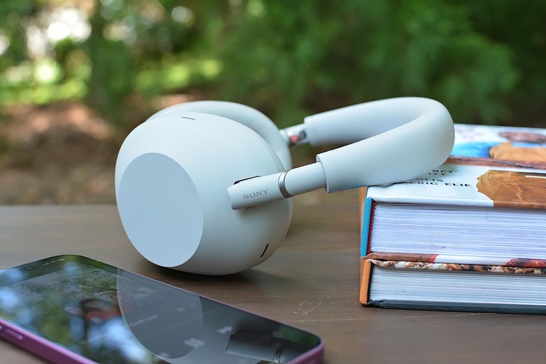 A white pair of Sony over-ear headphones leaning on a stack of books next to an iPhone.