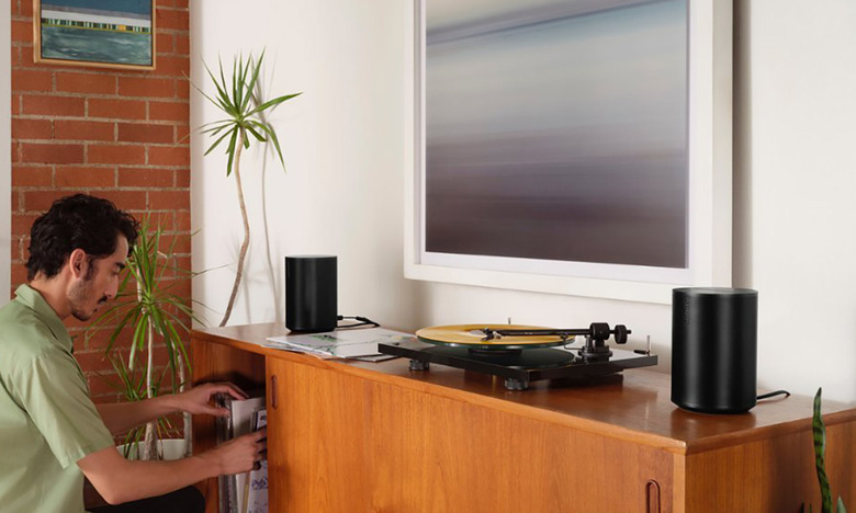 Two Sonos Era 100 speakers sit on a cabinet next to a turntable
