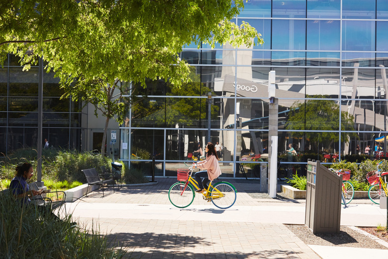 A  person riding a bike in front of a building with a mirror facade.