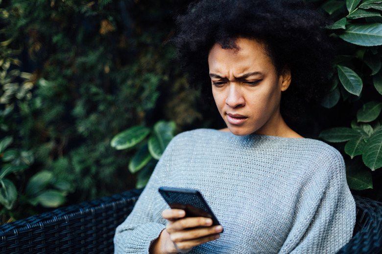 Young African American woman reading some bad news at home on her smart phone app, having a worried look on her face