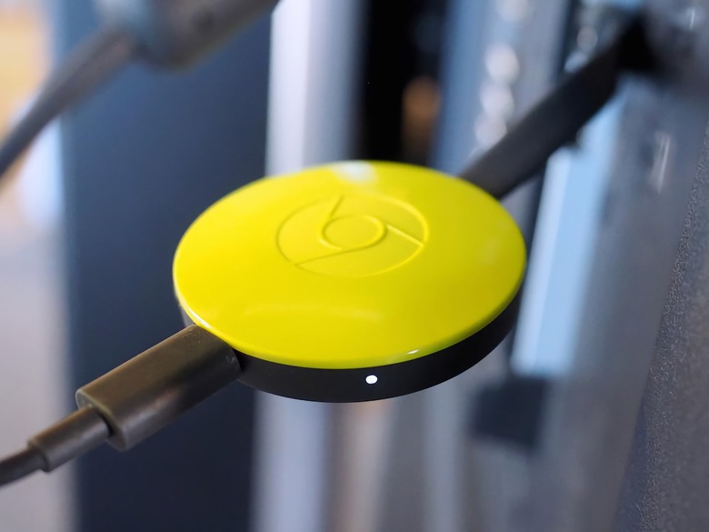 A yellow second-generation Chromecast plugged in to a TV.