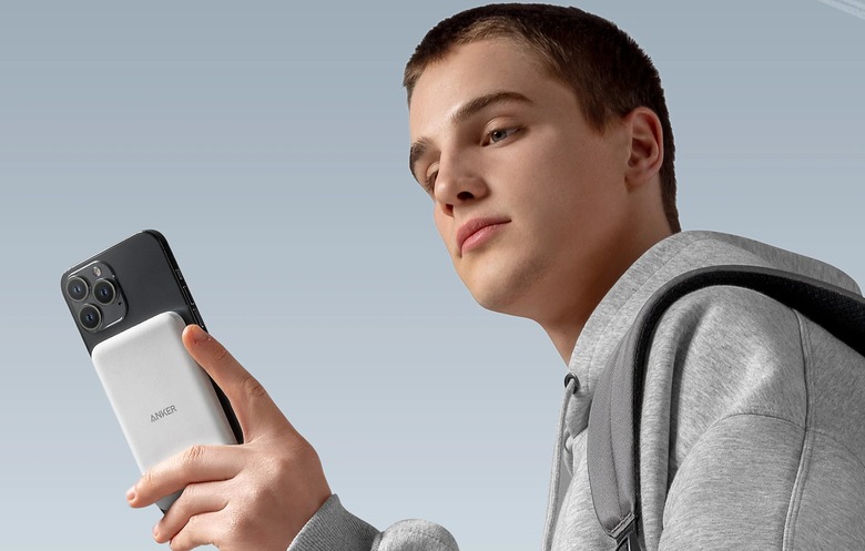 A person holding an iPhone with a MagSafe-compatible Anker charger attached.