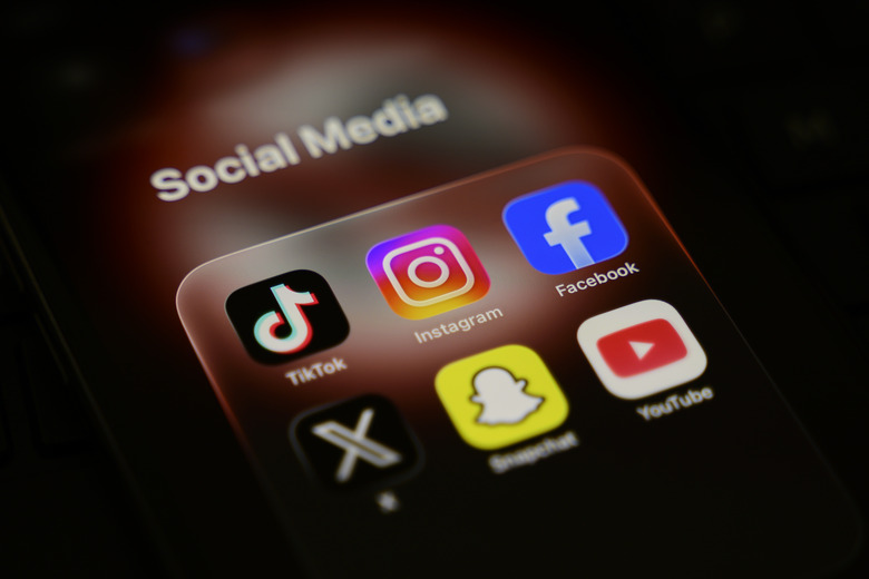 A smartphone displays a folder of social media applications, including TikTok, Instagram, Facebook, X, Snapchat, and YouTube, with a blurred ''no under-16'' sign in the background, in Creteil, France, on March 31, 2026. Australia's eSafety Commission warns social media platforms about their failure to enforce the country's ban on under-16 users. (Photo by Samuel Boivin/NurPhoto via Getty Images)